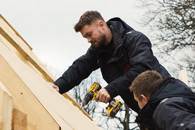 To tømrere fra Nemovo skruer lægter fast på en tagkonstruktion med en skruemaskine